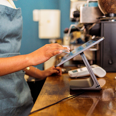 Barista using a touchscreen EPOS system at a café counter.