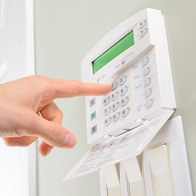 Hand pressing the buttons on a white alarm system keypad on a wall.
