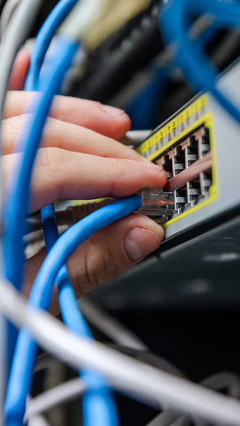 A hand connecting blue network cabling into a switch in a structured cabling setup.