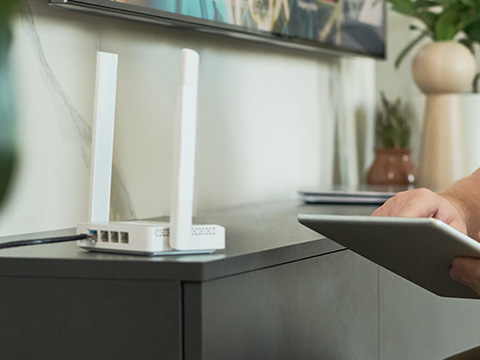 Router with two antennas on a cabinet, person holding a tablet nearby.