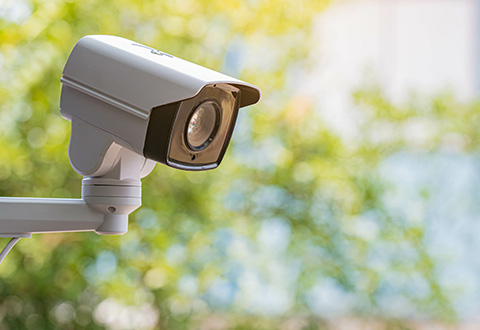 Outdoor CCTV camera mounted on a wall with a blurred green background.
