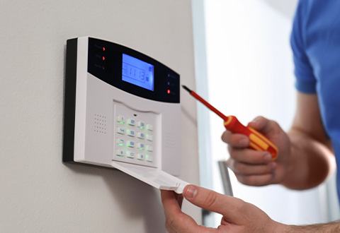 Installing a residential alarm system control panel with a screwdriver.