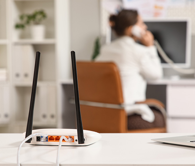 Router on a desk with Ethernet cables, while a person talks on the phone in the background.
