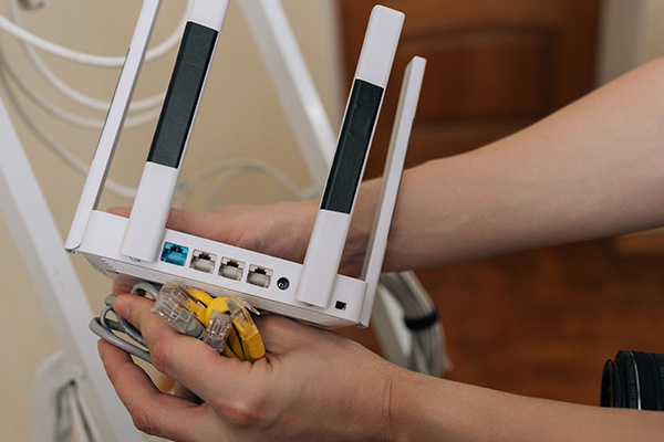 Hands holding a Wi-Fi router with Ethernet cables, illustrating home network installation.