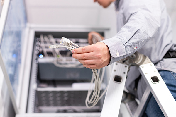 Technician installing network cables from a ladder in a server cabinet.