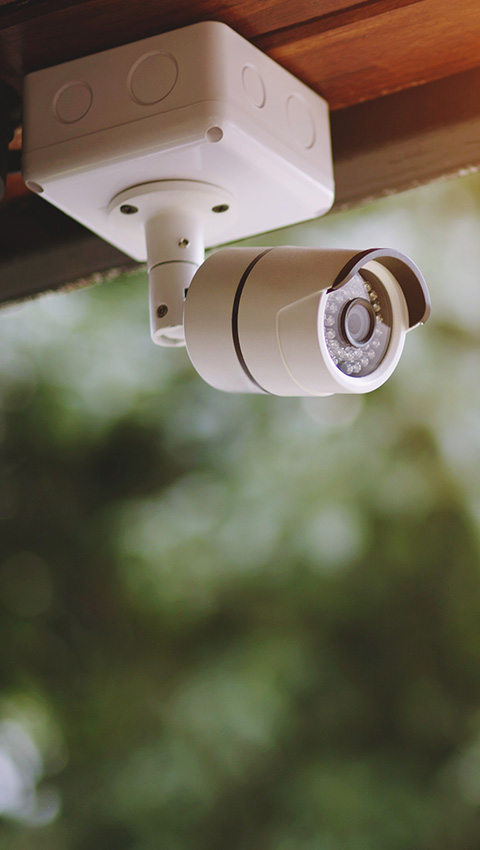 White CCTV camera mounted on a wall with a blurred green background.