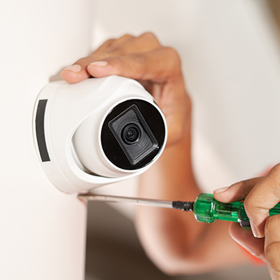 Installing a white CCTV camera on a wall with a screwdriver.