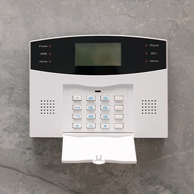 Security alarm control panel with keypad on a stone surface.