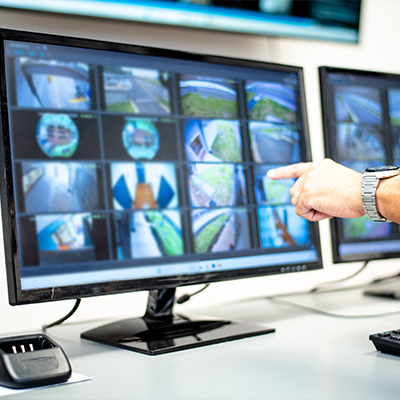 CCTV monitoring system displayed on a computer screen with a hand pointing at footage