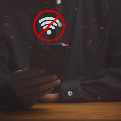 Hand holding a smartphone displaying a no Wi-Fi icon against a dark background.