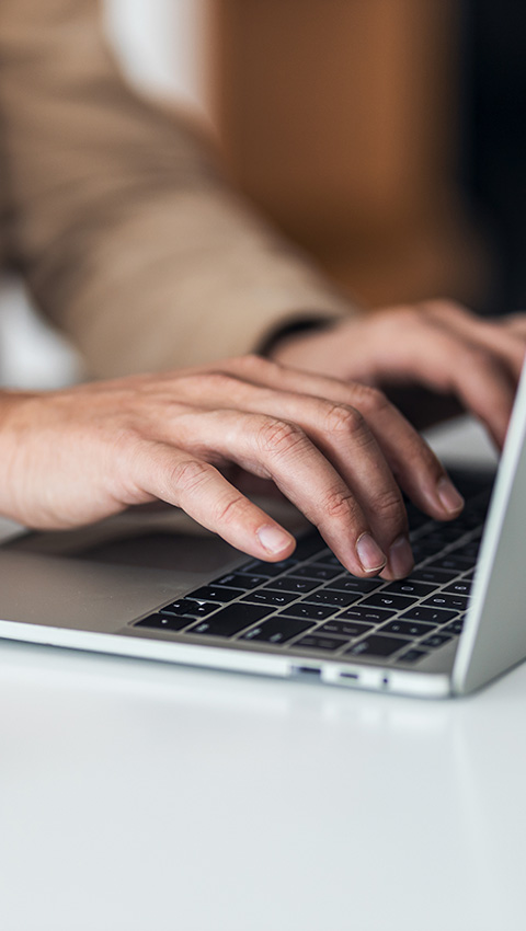 Hands typing on a laptop keyboard on a clean white surface.