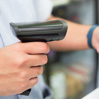 Hand holding a barcode scanner, focused on scanning an item in a retail setting.
