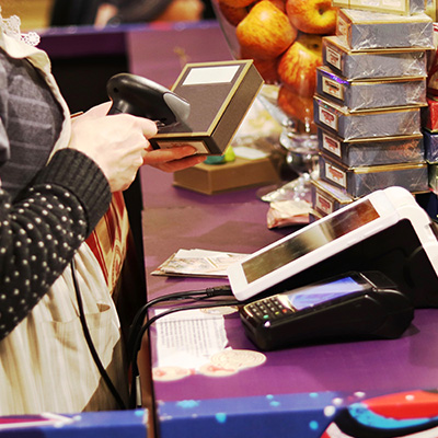 Cashier scanning a product at a retail checkout with a payment terminal and displayed items.